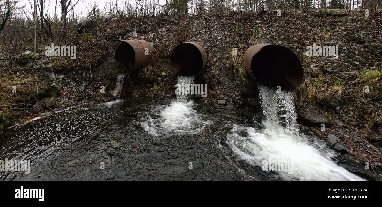 Tre tubi (tubo di drawndown) sotto una strada di campagna dike forniscono uno scarico di acqua da un piccolo fiume di foresta e stagno di deposito Foto Stock