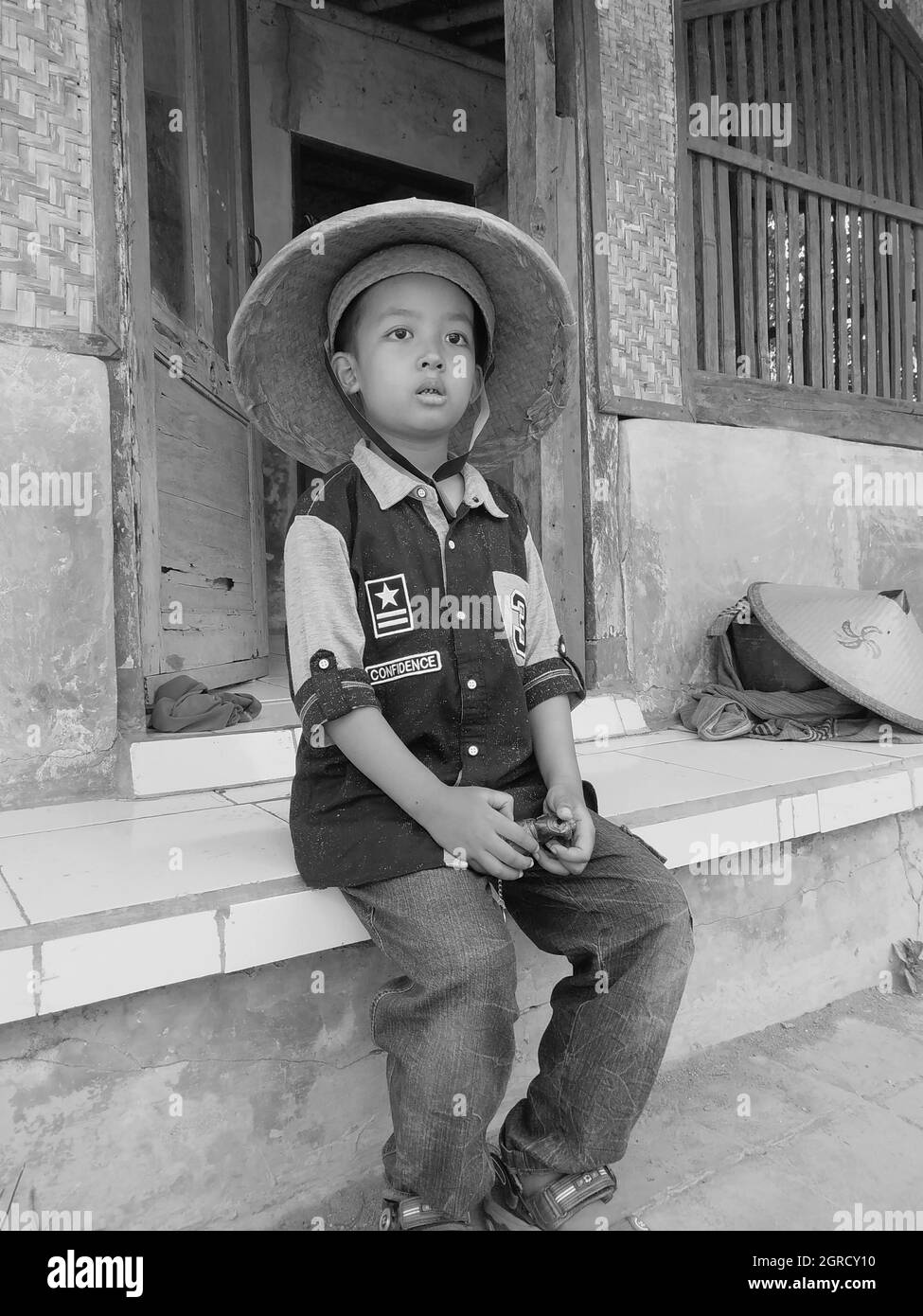 Ritratto bianco e nero di Innocent Boy con cappello da contadino  indonesiano Traditional seduto contro il muro Foto stock - Alamy