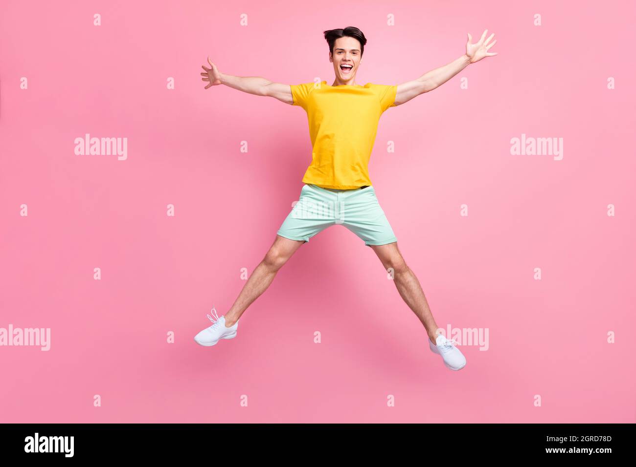 Foto di simpatico giovane uomo indossare giallo t-shirt jumping alto come stella isolato colore rosa sfondo Foto Stock