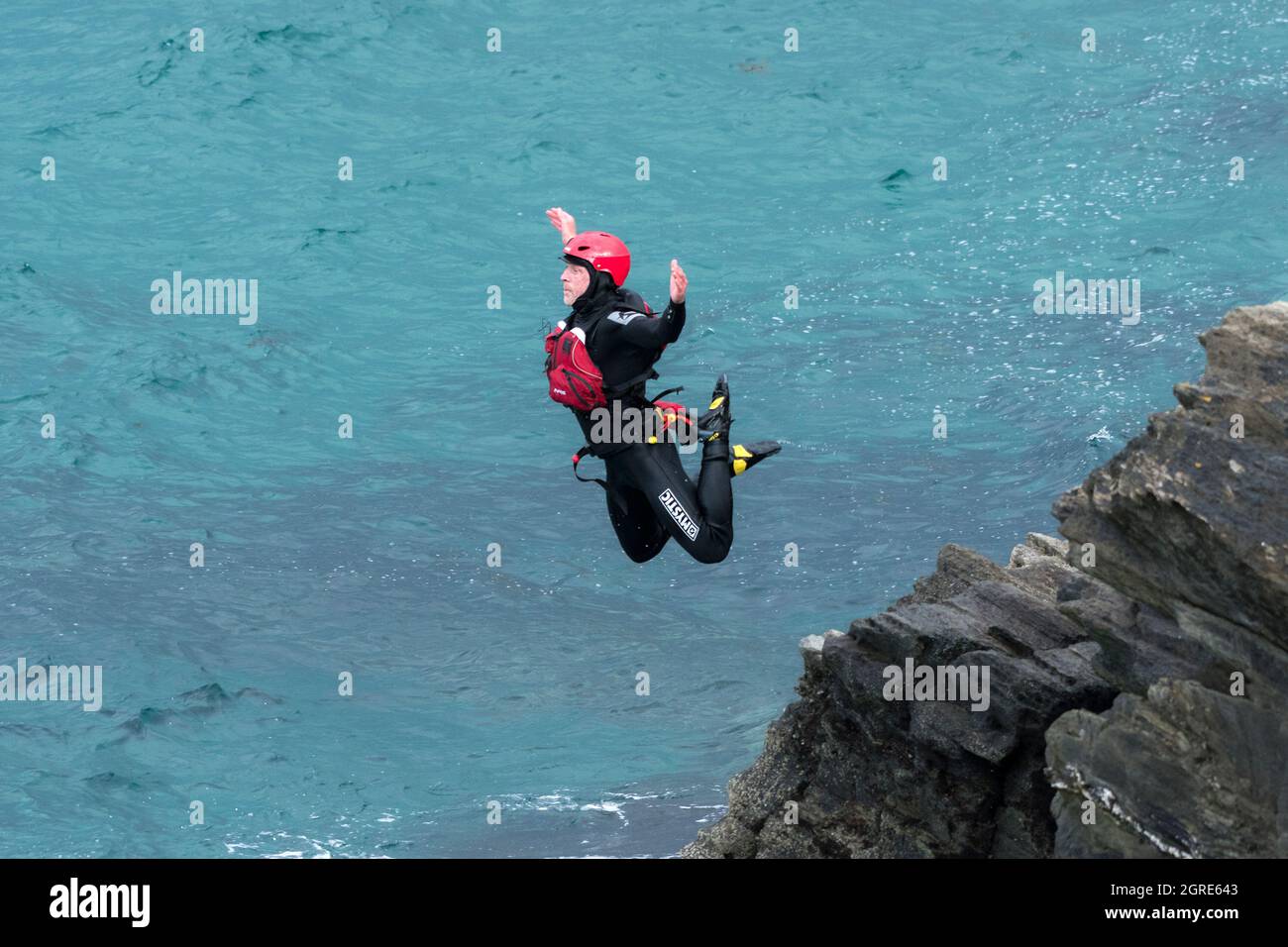Un istruttore di guida che dimostra come saltare dalle rocce durante un viaggio in coastering intorno a Towan Head a Newquay in Cornovaglia. Foto Stock