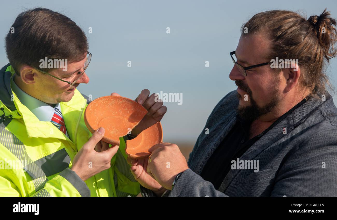 Deiningen, Germania. 01 ottobre 2021. Il direttore dell'area dell'Ufficio di Stato bavarese per la conservazione dei monumenti, Johann Friedrich Tolksdorf (l), e l'archeologo Manfred Woidlich tenere una ciotola di ceramica con incisioni. Durante gli scavi nella Nördlinger Ries, gli archeologi hanno trovato questa ciotola, che proviene dall'Africa, in una tomba del VI secolo, insieme ad altri beni sepolti. Credit: Stefan Puchner/dpa/Alamy Live News Foto Stock