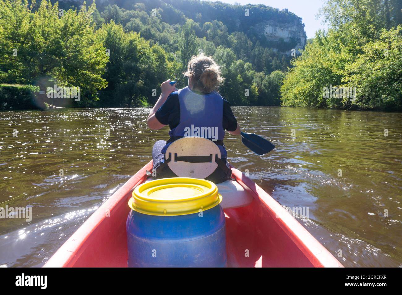 Vista posteriore di una donna che indossa un giubbotto salvagente che si addica una canoa lungo un fiume in europa Foto Stock