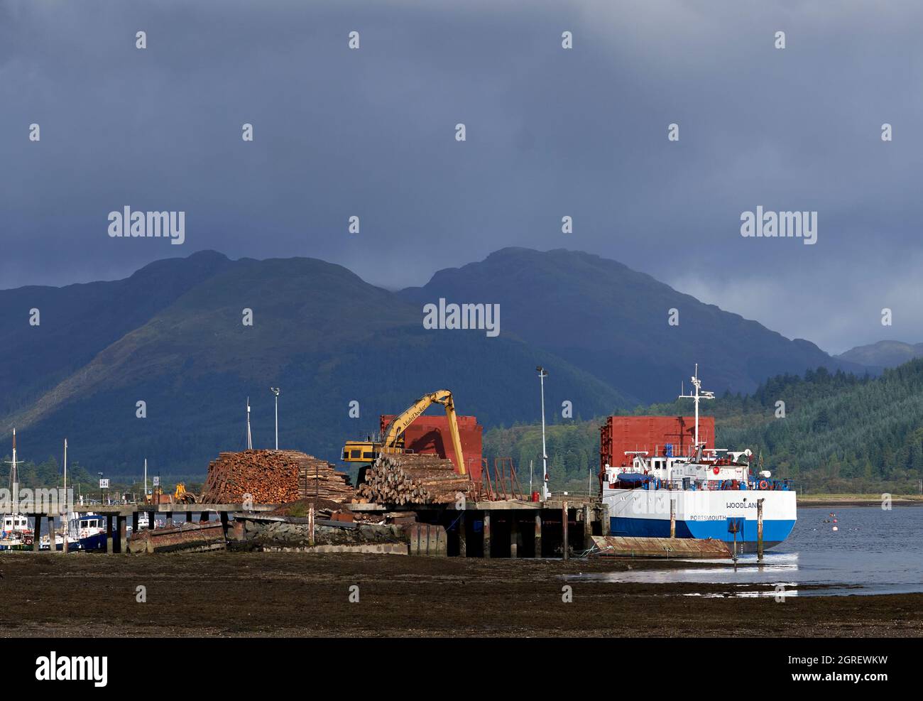 La barca ormeggiata a Dunoon è stata caricata con legname dalla Foresta Argyll raffigurata sullo sfondo. Foto Stock