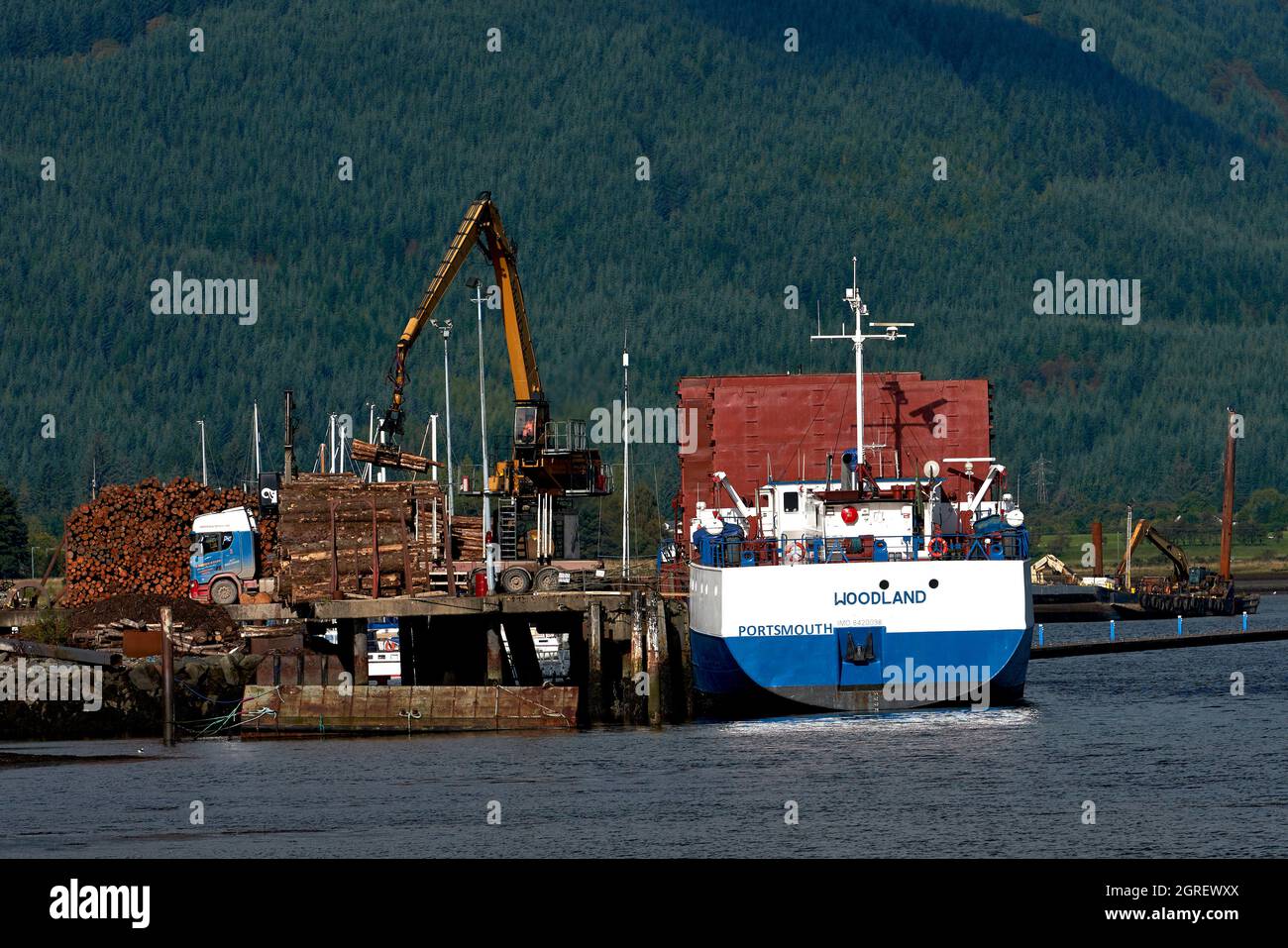 La barca ormeggiata a Dunoon è stata caricata con legname dalla Foresta Argyll raffigurata sullo sfondo. Foto Stock
