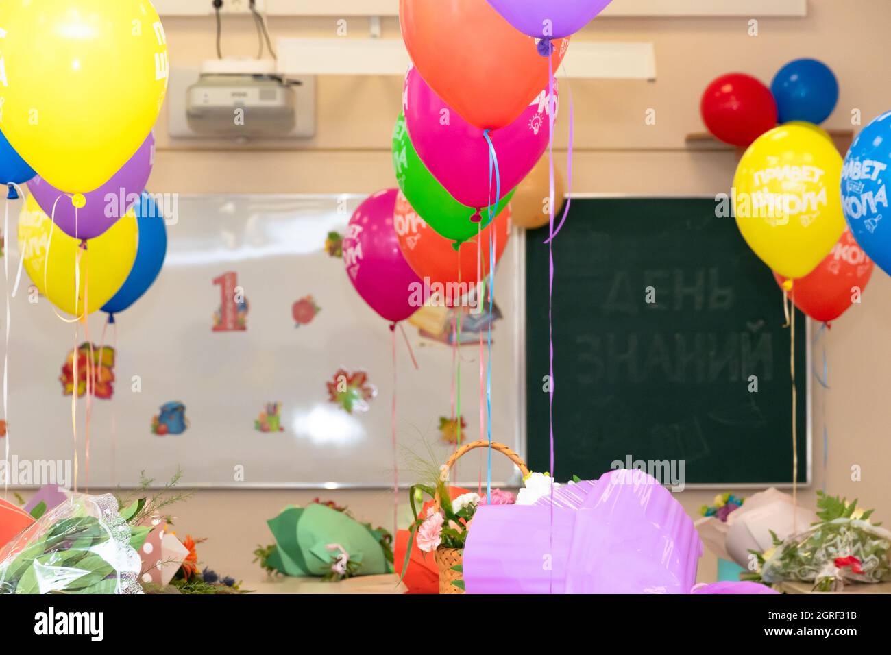 Lezione di scuola il 1 settembre senza studenti con palloncini colorati e fiori su scrivanie sullo sfondo del consiglio di scuola. Le iscrizioni Foto Stock