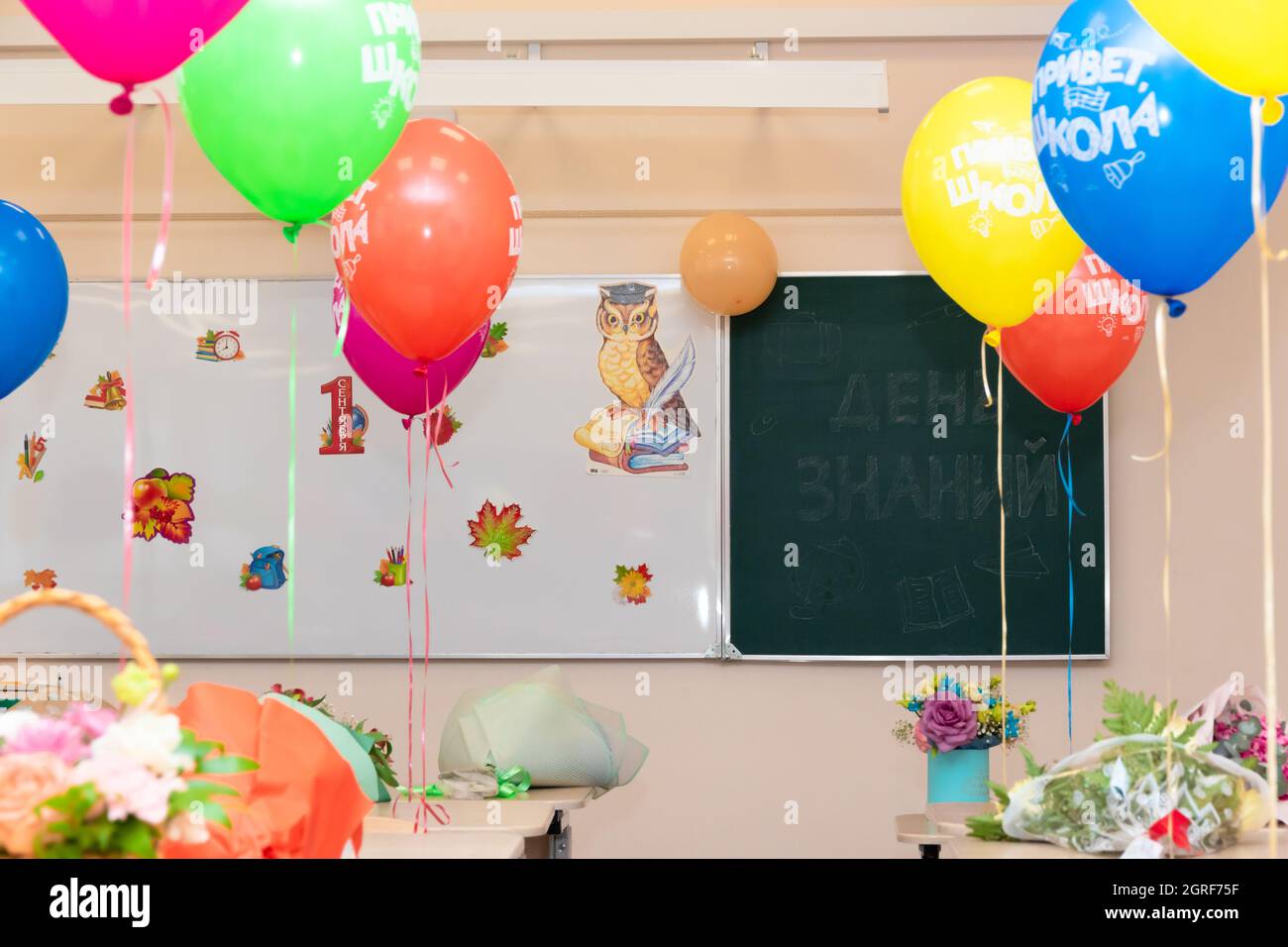 Lezione di scuola il 1 settembre senza studenti con palloncini colorati e fiori su scrivanie sullo sfondo del consiglio di scuola. Le iscrizioni Foto Stock