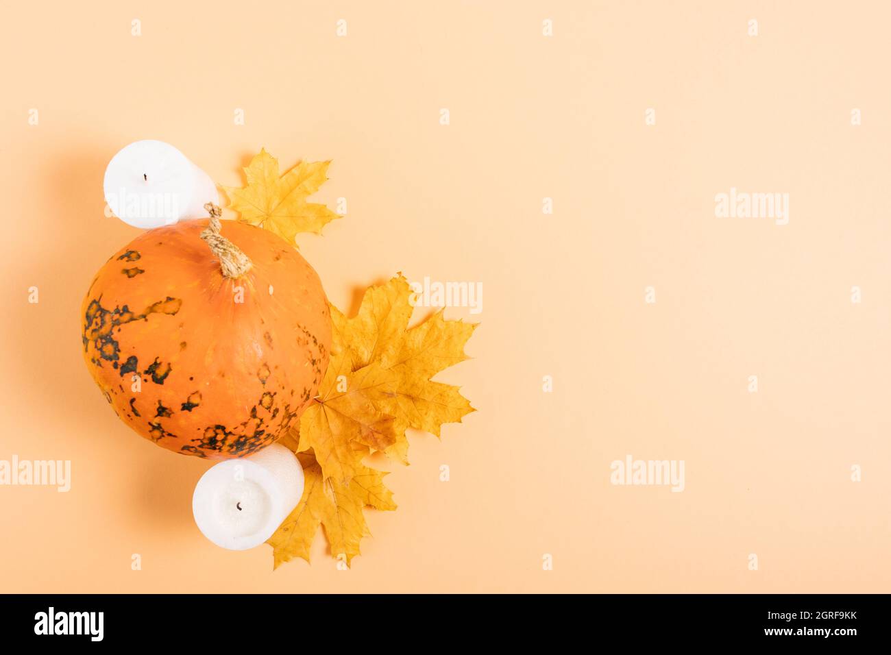 Decorazione autunnale con zucca, foglie gialle e candele su sfondo arancione chiaro, piatto. Foto Stock