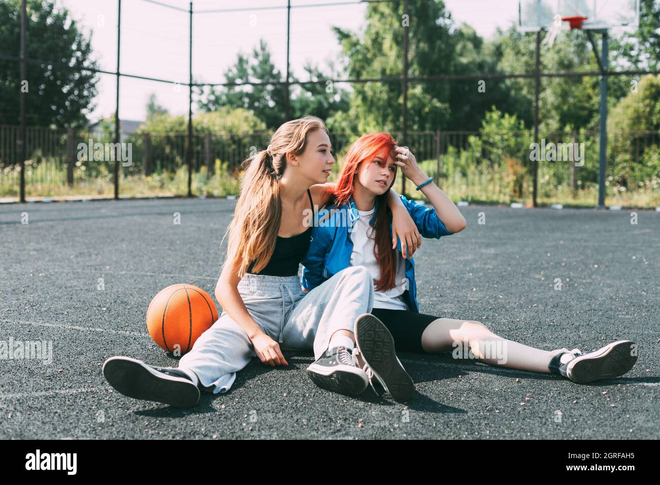 Due ragazze in abiti sportivi e con Un basket stanno chiacchierando, seduti  sul parco giochi. Sport Foto stock - Alamy