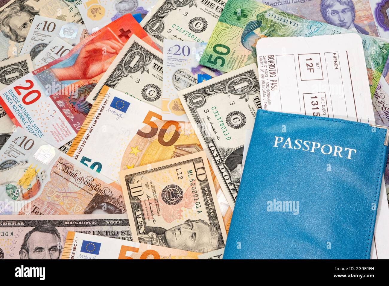 Biglietto aereo e passaporto posati sopra molte banconote in valuta mondiale Foto Stock