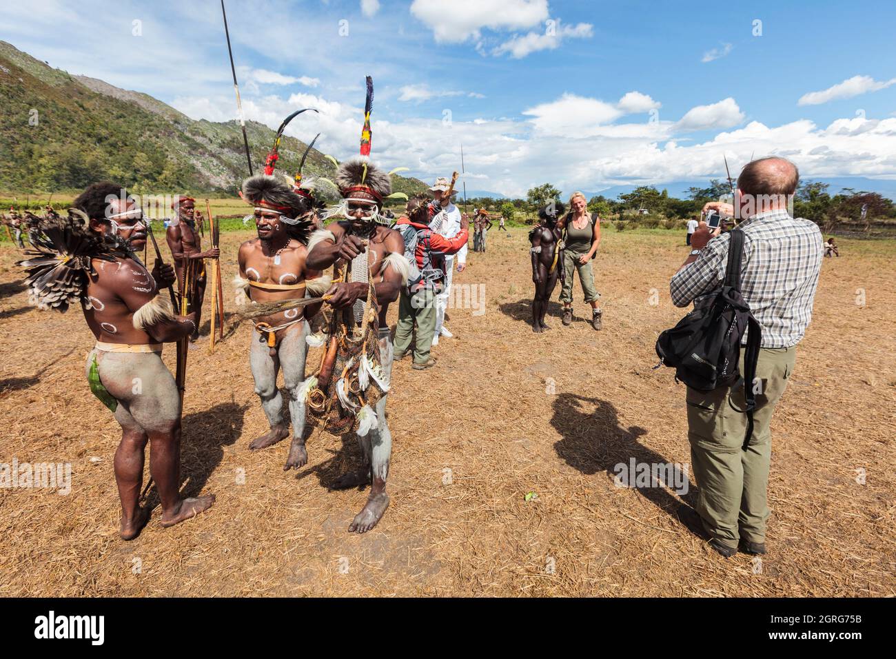 Indonesia, Papua, la città di Wamena, turisti occidentali fotografando se stessi con tribù locali. Baliem Valley Cultural Festival, ogni agosto, le tribù si riuniscono per eseguire scene di guerra ancestrali, sfilate e danze in abiti tradizionali Foto Stock