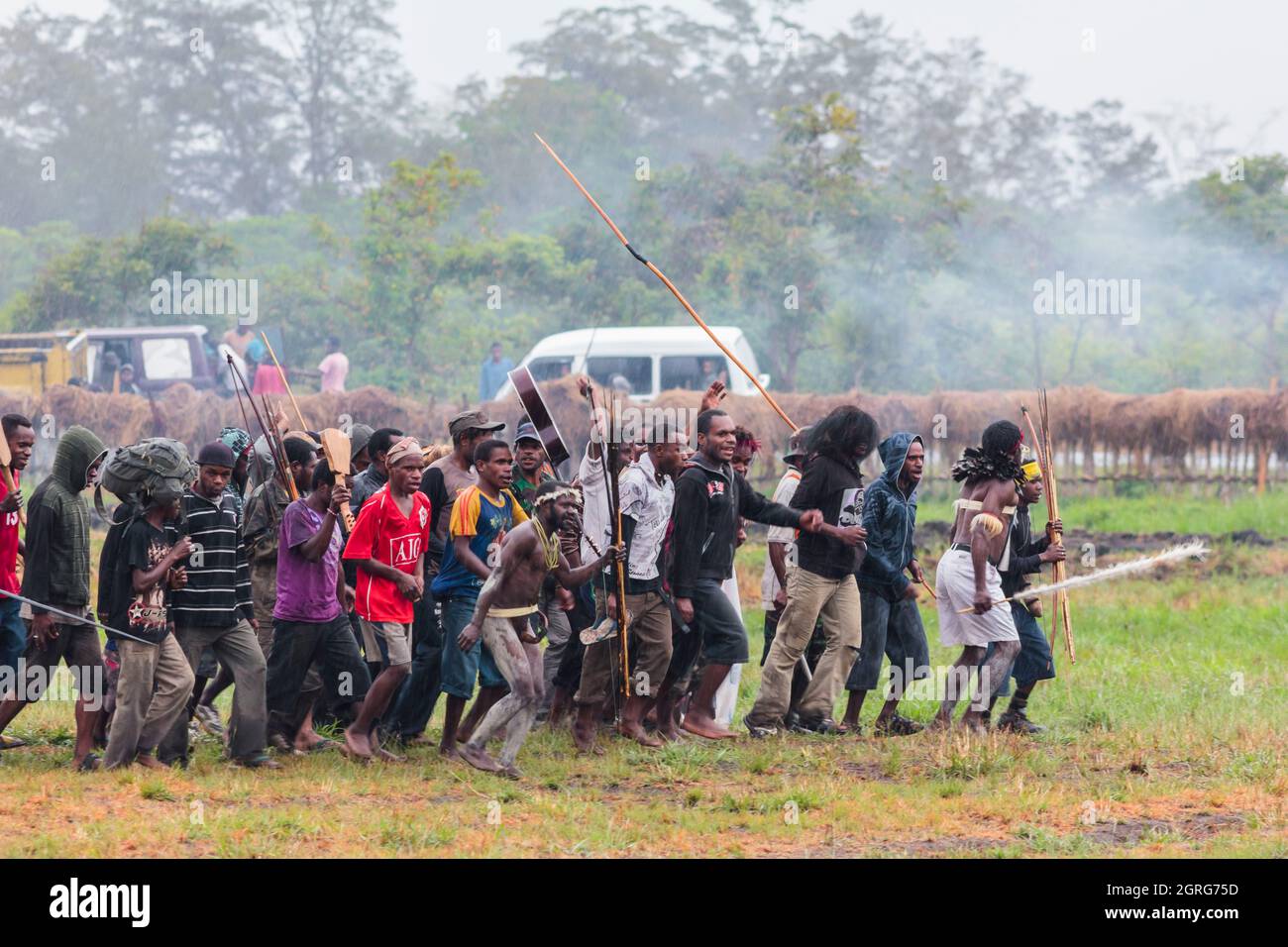 Indonesia, Papua, città di Wamena, gruppo di uomini della tribù Dani, che provano una scena di guerra tribale, sotto la pioggia. Baliem Valley Cultural Festival, ogni agosto, le tribù si riuniscono per eseguire scene di guerra ancestrali, sfilate e danze in abiti tradizionali Foto Stock