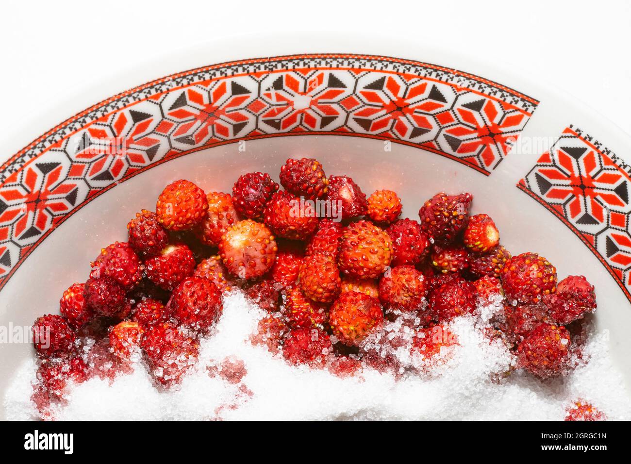 Fragole selvatiche (Fragaria vesca) con cristalli di zucchero, su una ciotola con motivi etnici rumeni. Foto Stock