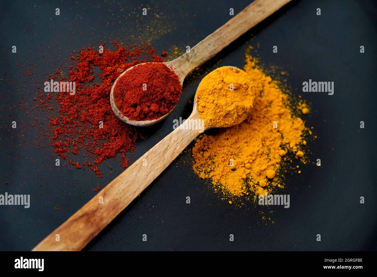 due cucchiai di legno con paprika affumicata e curcuma, isolati su un piattino nero Foto Stock