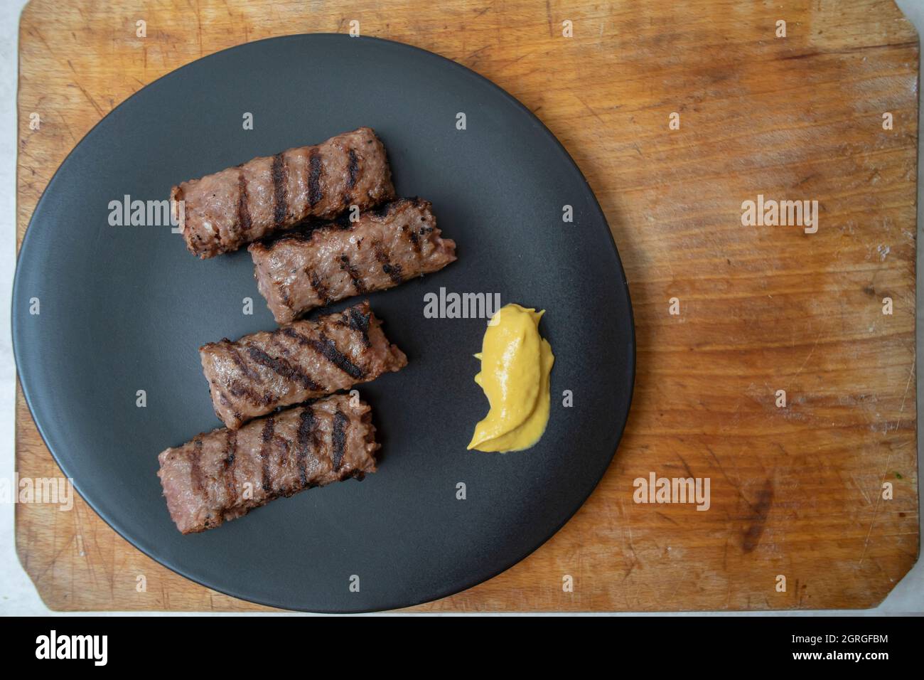 Carne tritata alla griglia tradizionale rumena, mici o mititei su un piatto di ceramica nera con senape Foto Stock