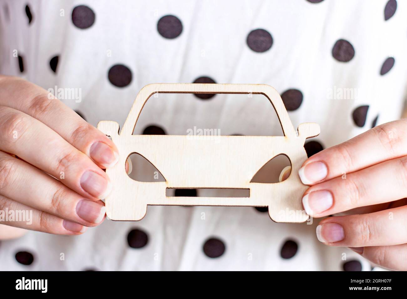 Mini giocattolo bianco in legno per auto in donna caucasica mani su sfondo chiaro. Assicurazione auto, affitto, vendita e concetto di servizio. Foto Stock