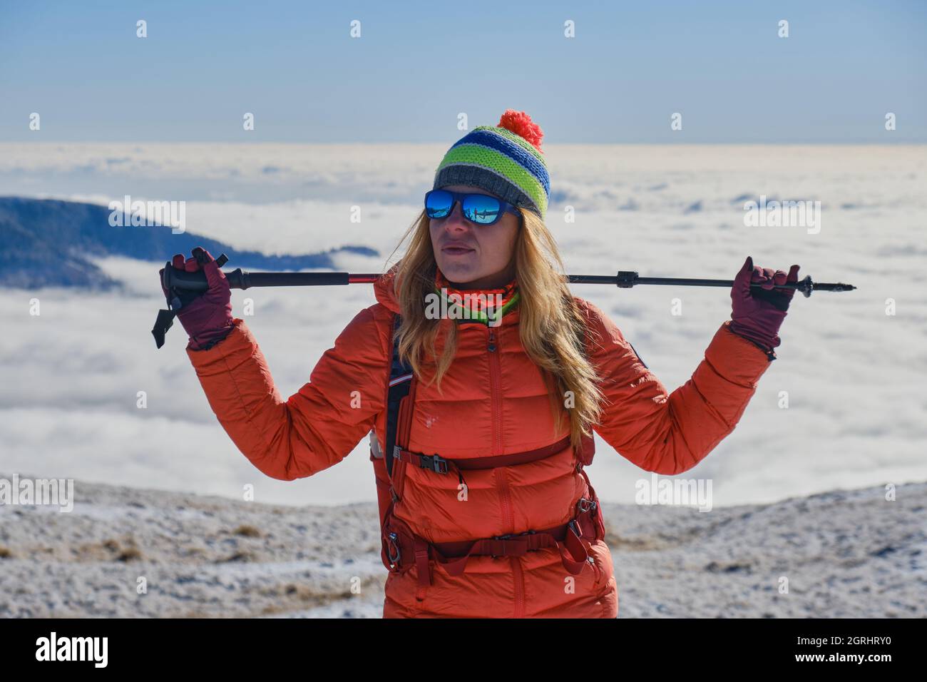Donna escursionista con abbigliamento sportivo invernale e palo da trekking, guarda lontano, contro una valle piena di nuvole. Attività invernali sui monti Carpazi, Foto Stock