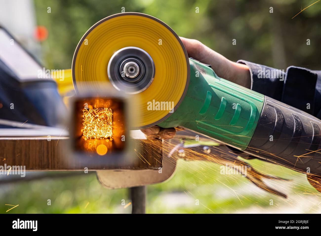Un'immagine messa a fuoco di una smerigliatrice per saldatura utilizzata da una donna , che corre su una superficie metallica, in un ambiente esterno, scintille di fuoco possono essere viste volare intorno. Foto Stock