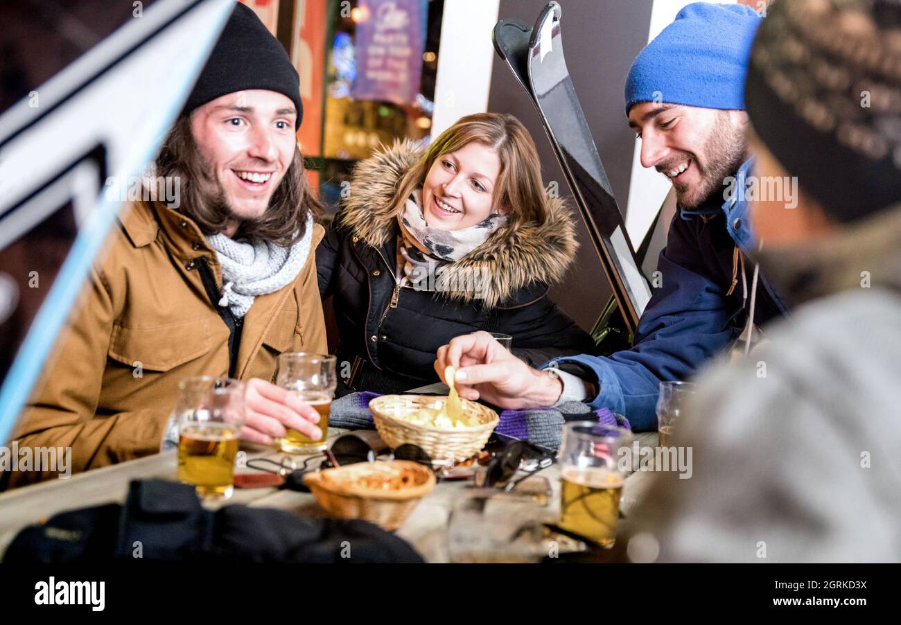 Happy amici a bere birra e mangiare patatine - gente allegra divertirsi presso il bar ristorante dal centro sciistico con neve attrezzatura - Il concetto di amicizia Foto Stock