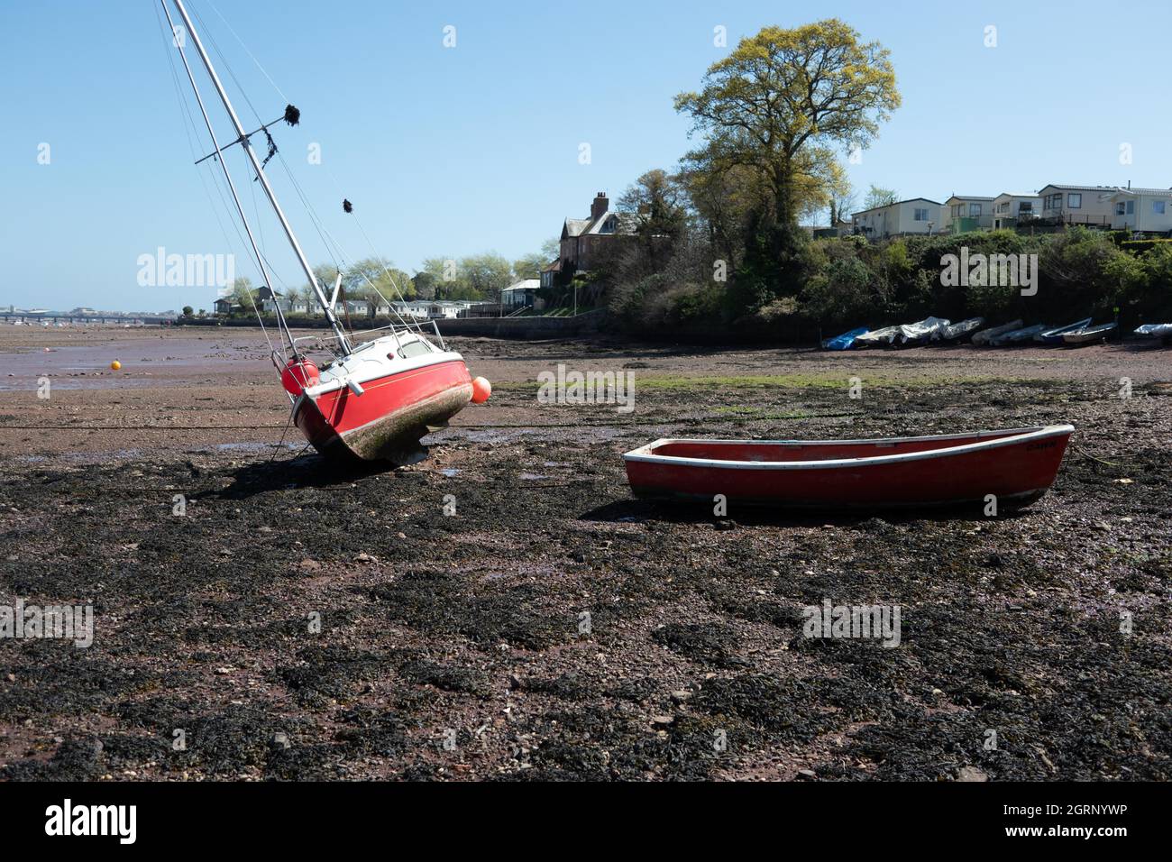 Piccolo yacht rosso e barca a remi aground a bassa acqua nel fiume Teign estuario vicino Teignmouth Sud Devon Inghilterra Foto Stock