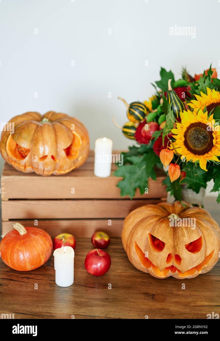 Concetto di festa d'autunno: Zucche, candele, girasole e altri attributi al tavolo come sfondo tema festa di Halloween. Zucca d'arancia di Halloween con facce malvagie spaventose. Foto verticale di alta qualità Foto Stock