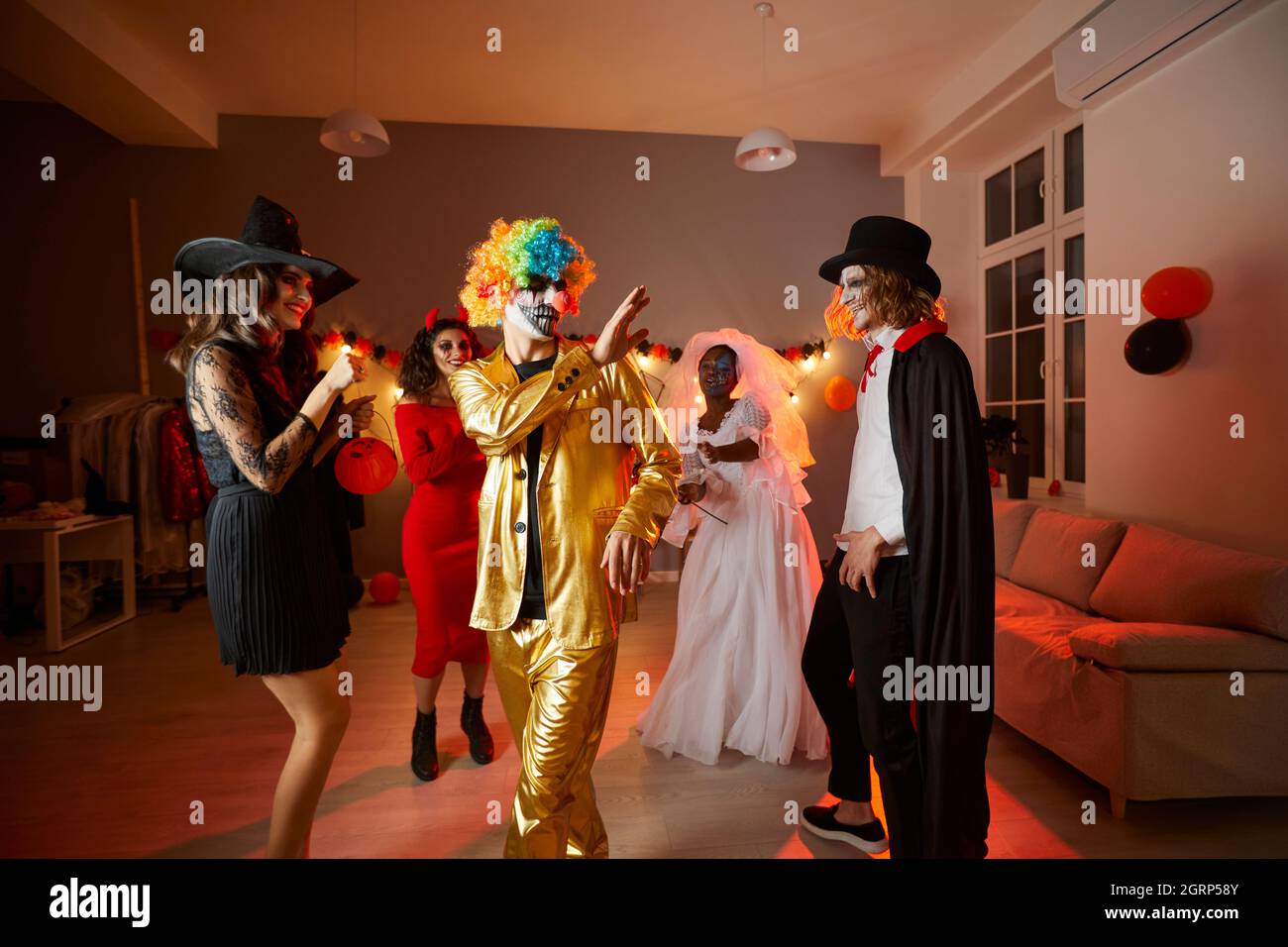 Amici giovani felici vestiti in costumi danzanti in una divertente festa di Halloween a casa Foto Stock