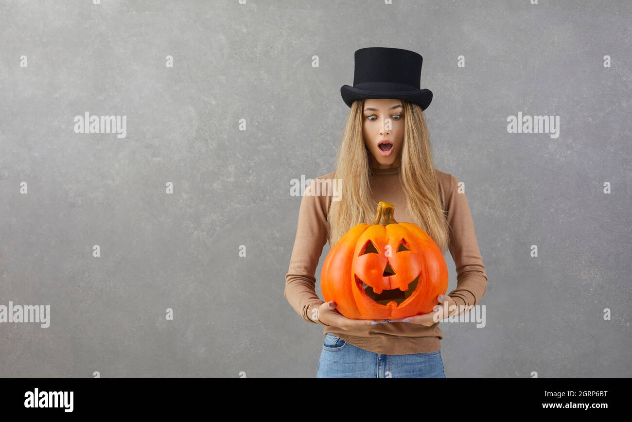 Donna sorpresa nel cappello superiore in piedi su sfondo copyspace e tenendo Halloween zucca Foto Stock