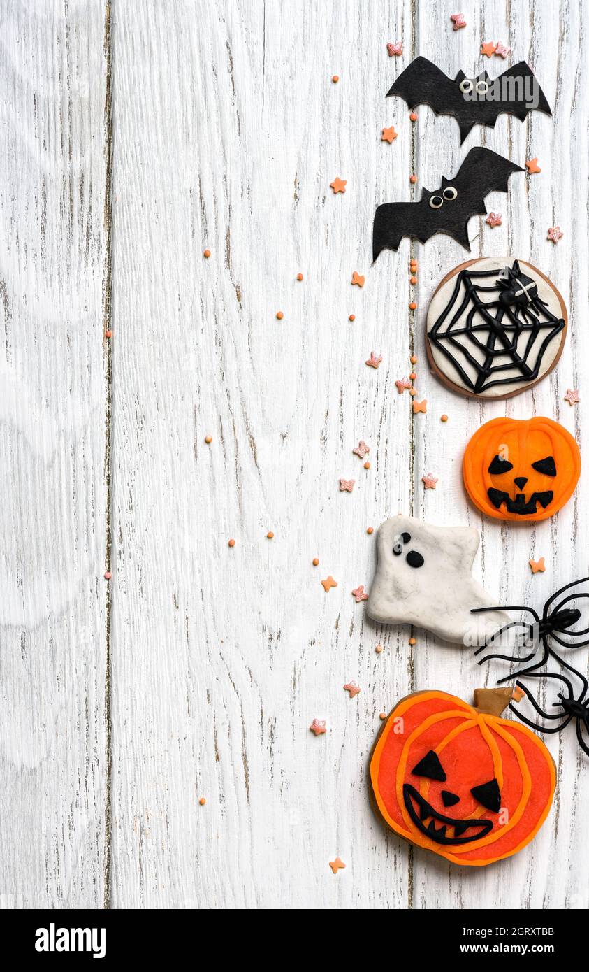 Halloween sfondo con biscotti, fantasma e pipistrelli, vista dall'alto. Oggetti divertenti di Halloween su tavola bianca in legno con spazio per il testo, disposizione piatta. Hallowen foo Foto Stock