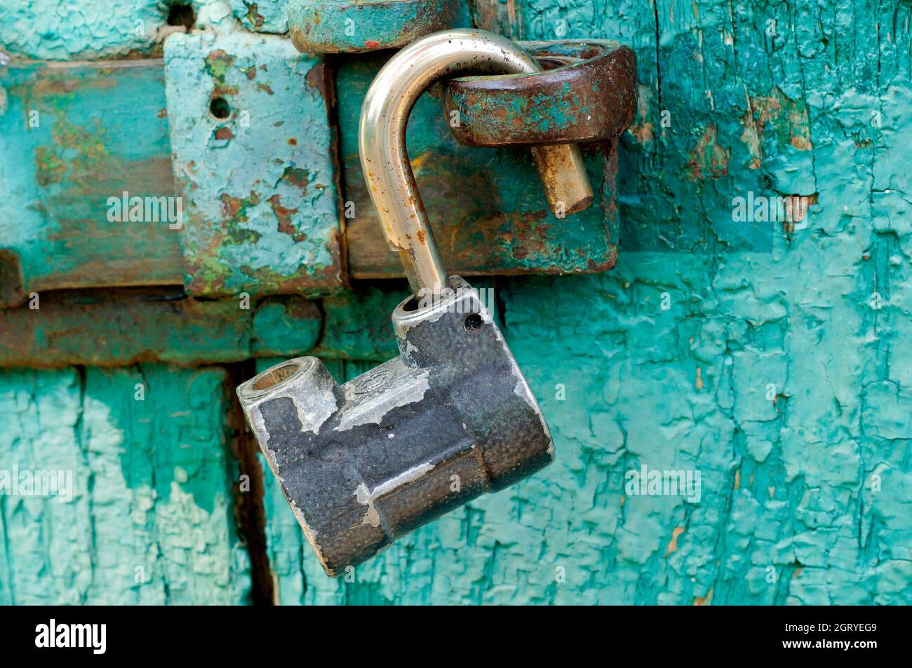 Lucchetto in acciaio aperto su una vecchia parete in teal verde e blu d'epoca con vernice sfolgnante Foto Stock
