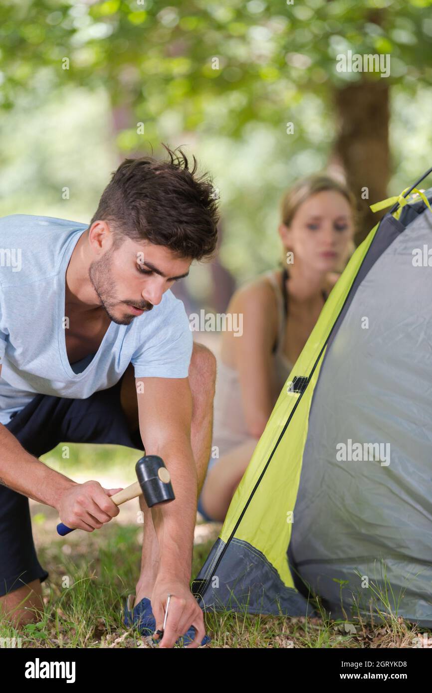 uomo che martellano i pioli della tenda dentro al terreno Foto Stock