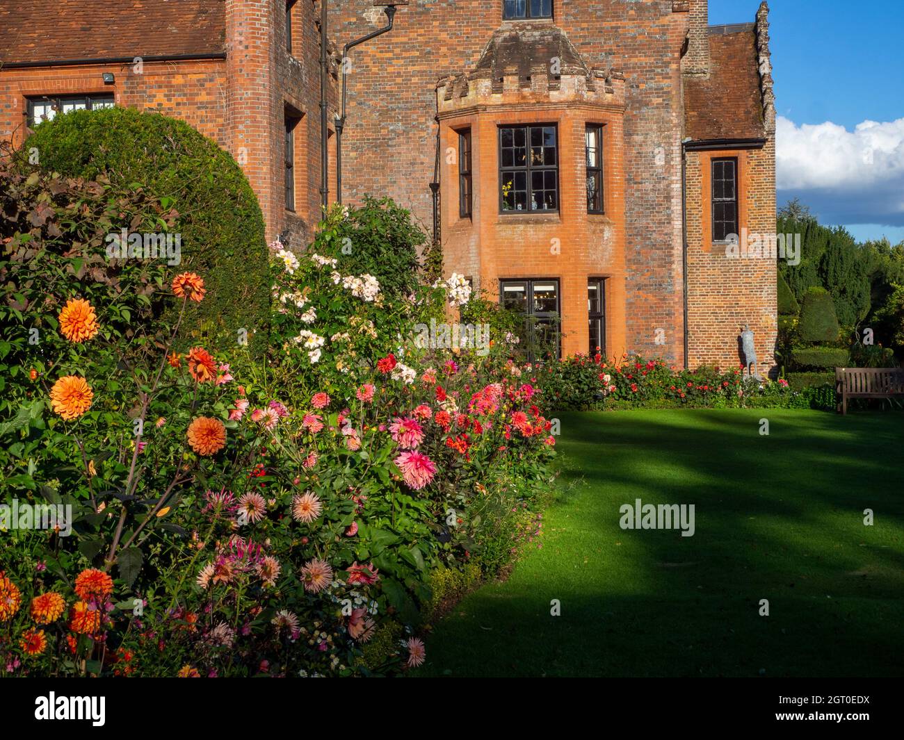 Chenies Manor House in Autumn.Plant confine con grandi fiori di dahlia arancione e rosa portare l'occhio alle finestre della baia del maniero Tudor nel mese di settembre. Foto Stock