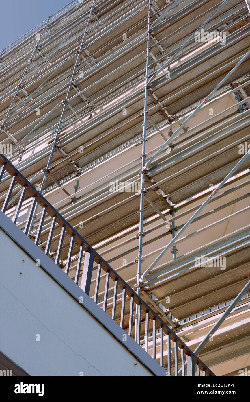 Un alto e moderno edificio e' circondato da impalcature in legno e alluminio tubolare durante un periodo di ristrutturazione strutturale. Foto Stock