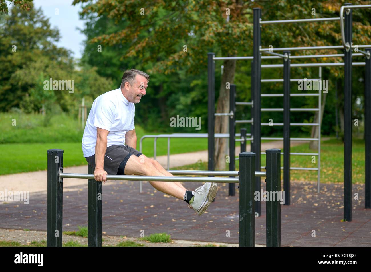Uomo anziano che si sta allenando su barre parallele all'aperto in un parco che si sospende con il braccio mentre rinforza e tonifica i suoi muscoli in una salute e in un fit Foto Stock