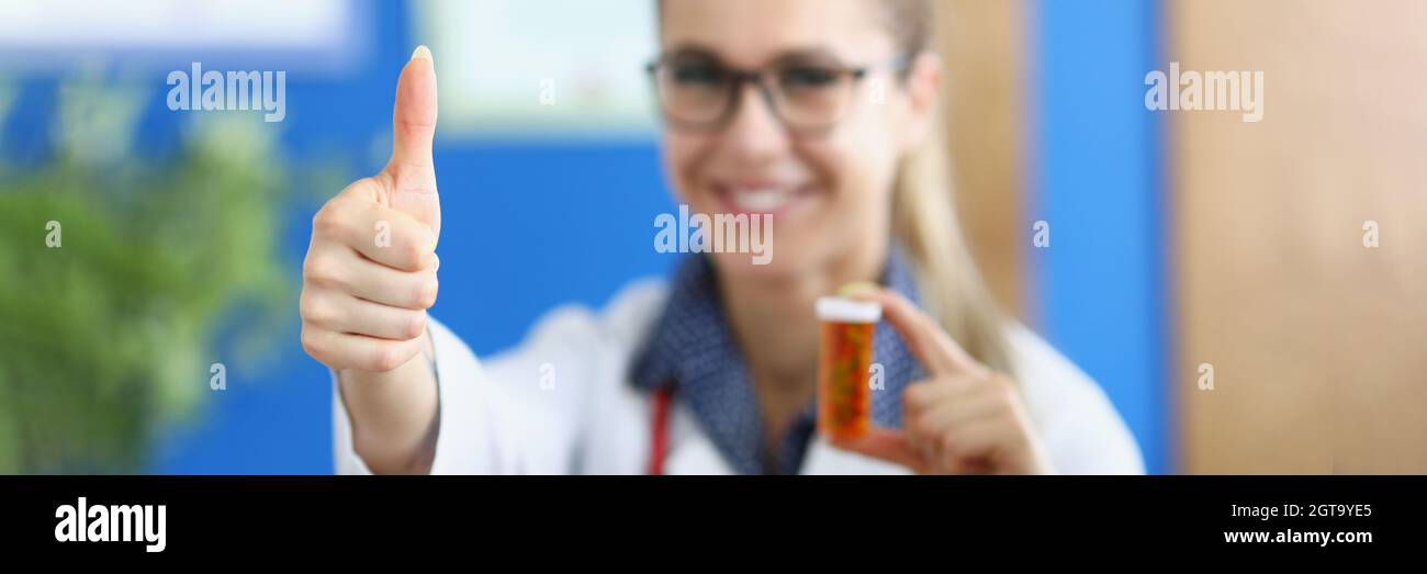 Donna sorridente medico mostrando pollici e tenendo in mano il farmaco Foto Stock