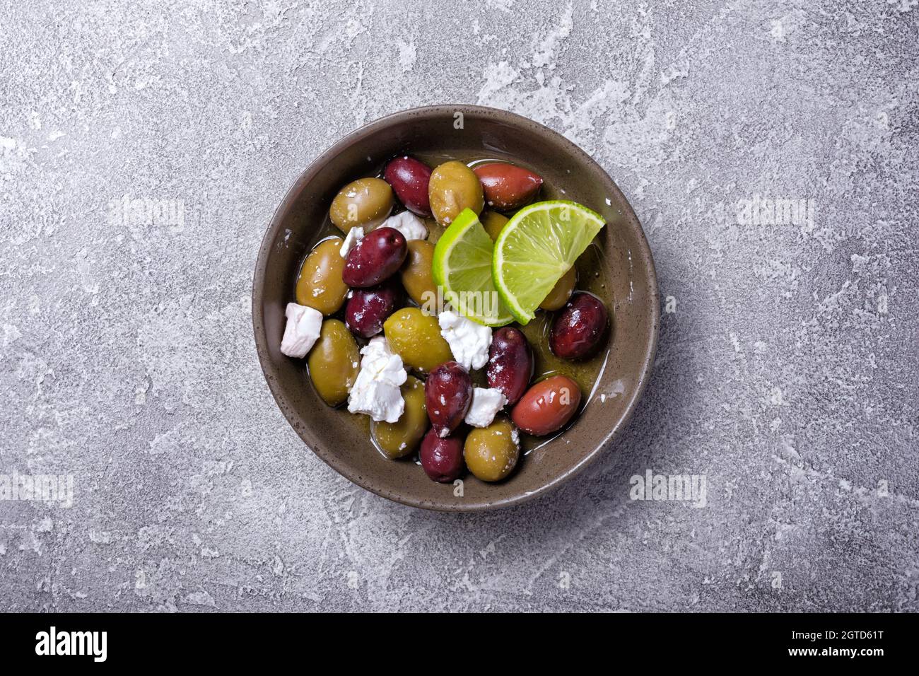 Vista dall'alto di gustose olive mescolate con formaggio Feta e fettine di lime su fondo grigio di cemento Foto Stock