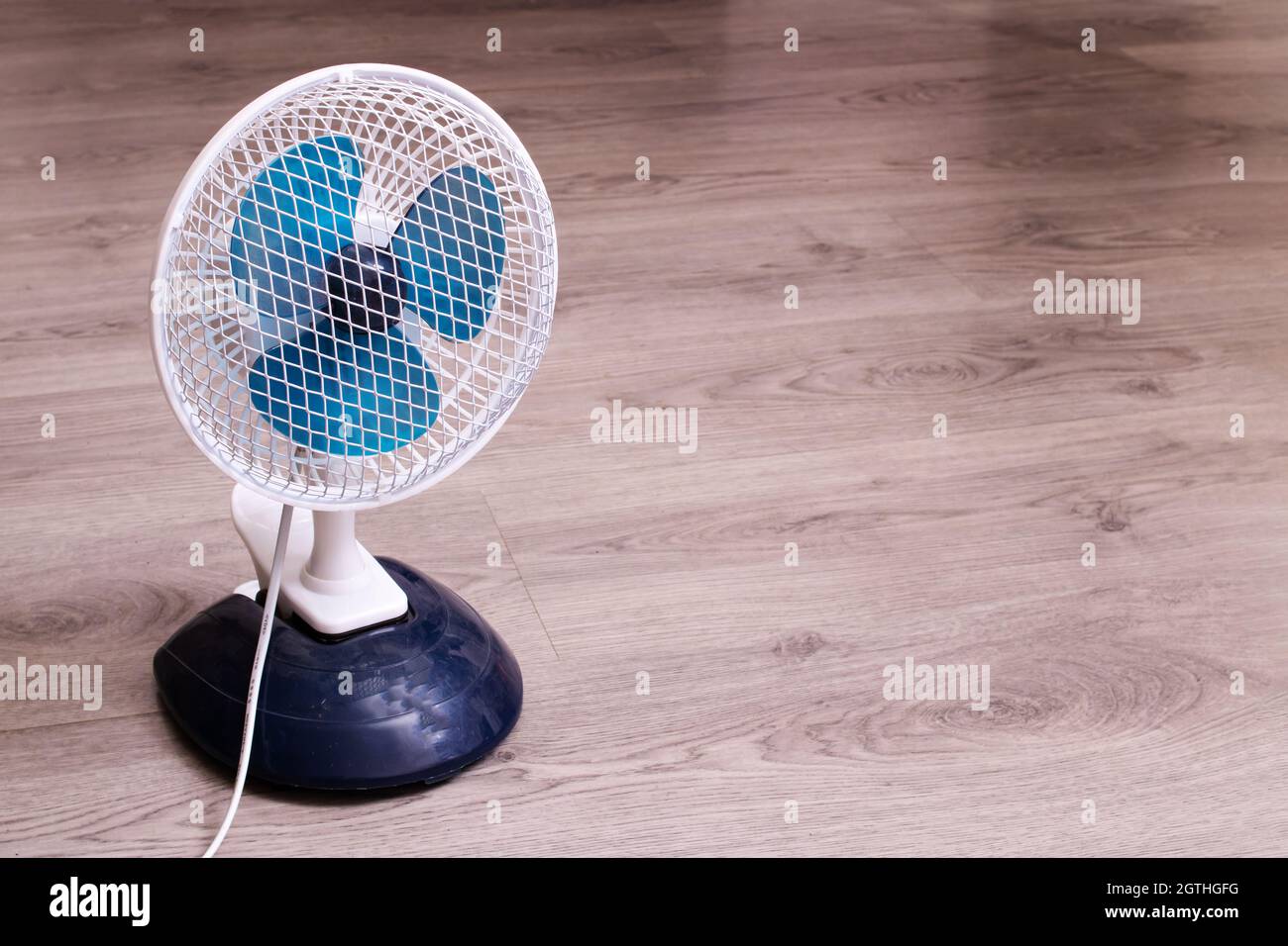 Piccolo ventilatore sul pavimento in legno in primo piano, spazio copia Foto Stock