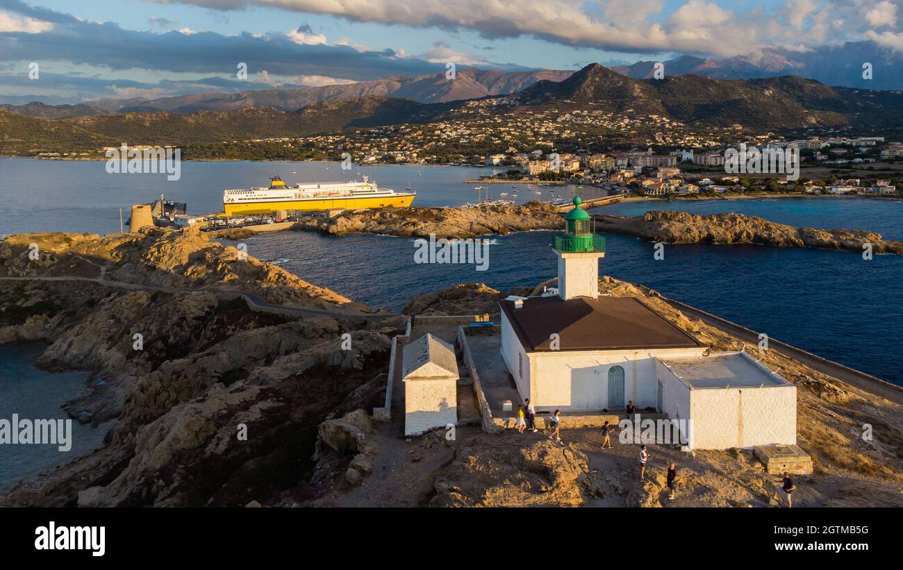 Veduta aerea del faro sull'isola di pietra con un traghetto giallo ormeggiato nel porto di Île Rousse sullo sfondo, Corsica Settentrionale, Francia - Foto Foto Stock