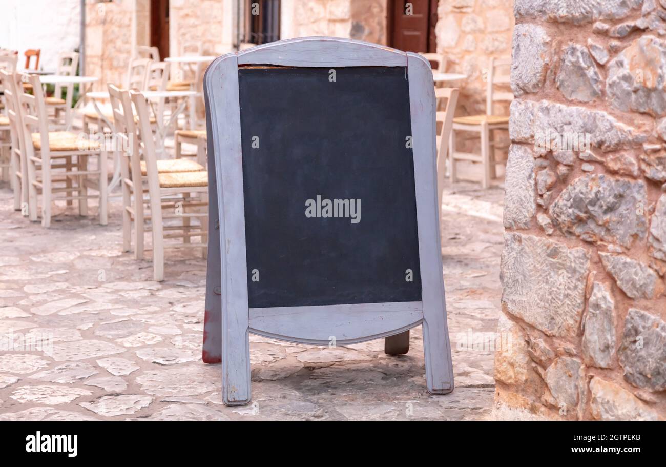 Menu. Lavagna bianca con telaio in legno all'aperto su un marciapiede lastricato in pietra. Oggi modello di menu, taverna tradizionale villaggio in Grecia, Foto Stock