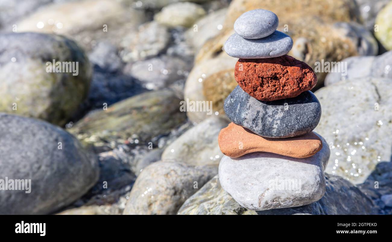 Pietre di equilibrio Zen, torre di ciottoli liscia accatastata su sfondo roccioso bagnato, giorno di sole sulla riva rocciosa. Armonia e pace sul mare Foto Stock