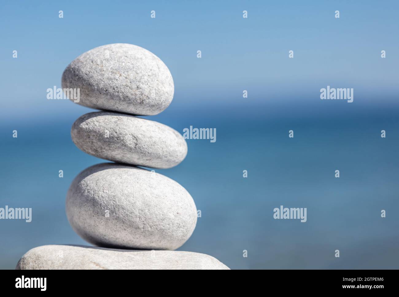 Equilibrio, pietre zen, piramide di ciottoli lisci accatastati su mare blu sfocato e cielo sfondo, giorno di sole. Feng shui, armonia e concetto di pace. Spazio copia, Foto Stock
