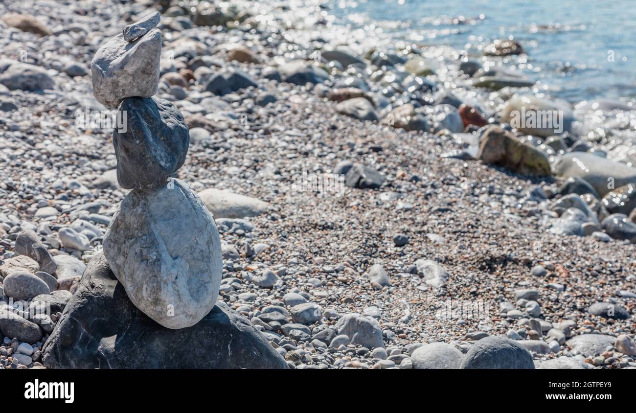 Feng shui, armonia e concetto di pace. Equilibrio, pietre zen, piramide rocciosa accatastata su spiaggia di ciottoli, sfondo blu mare, giorno di sole. Spazio di copia, modello. Foto Stock