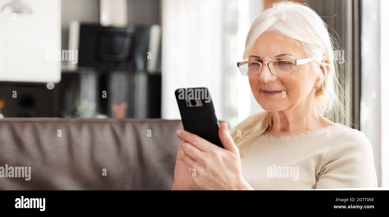 Bella donna senior texting a casa. Il titolare di pensione o di rendita utilizza social media Foto Stock