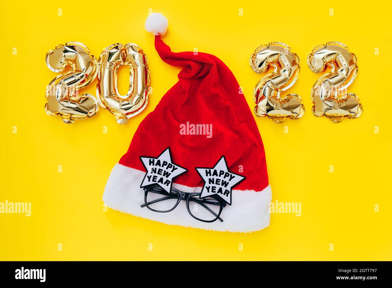 Palloncini in alluminio sotto forma di numeri 2022 e cappello Santa con occhiali da festa su sfondo giallo. Festa di capodanno. Foto Stock