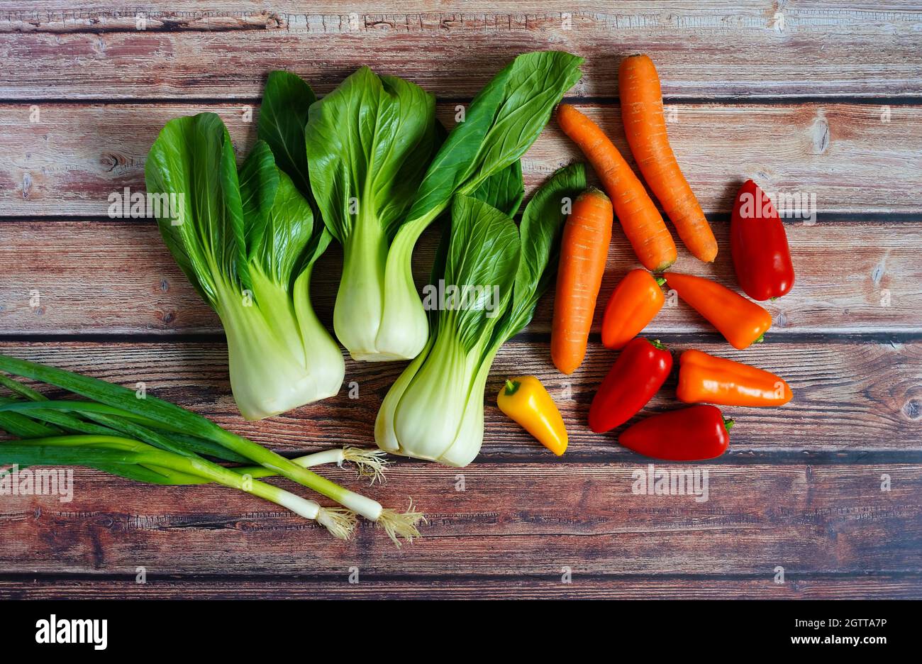 Cipolline fresche, pak choi, carote e peperone su un rustico tavolo in legno. Preparazione per una cucina casalinga sana per sostenere il sistema immunitario. Foto Stock