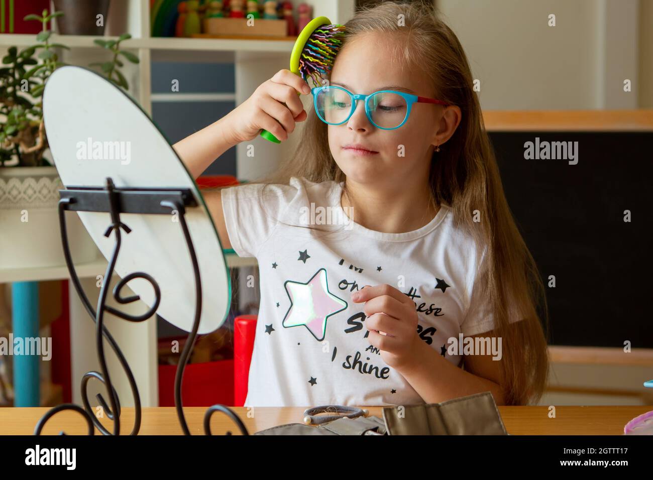 Bella ragazza con sindrome di Down pettinando i capelli di fronte a uno specchio a casa Foto Stock