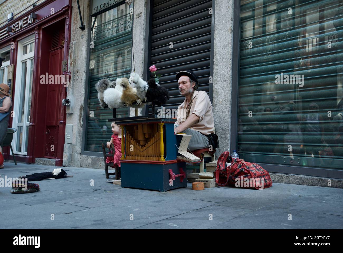 Busker che suona una scatola di musica basata su carte con polli a Rua das Flores, Porto - busker di strada portoghese che suona strumento d'organo con polli Silkie Foto Stock