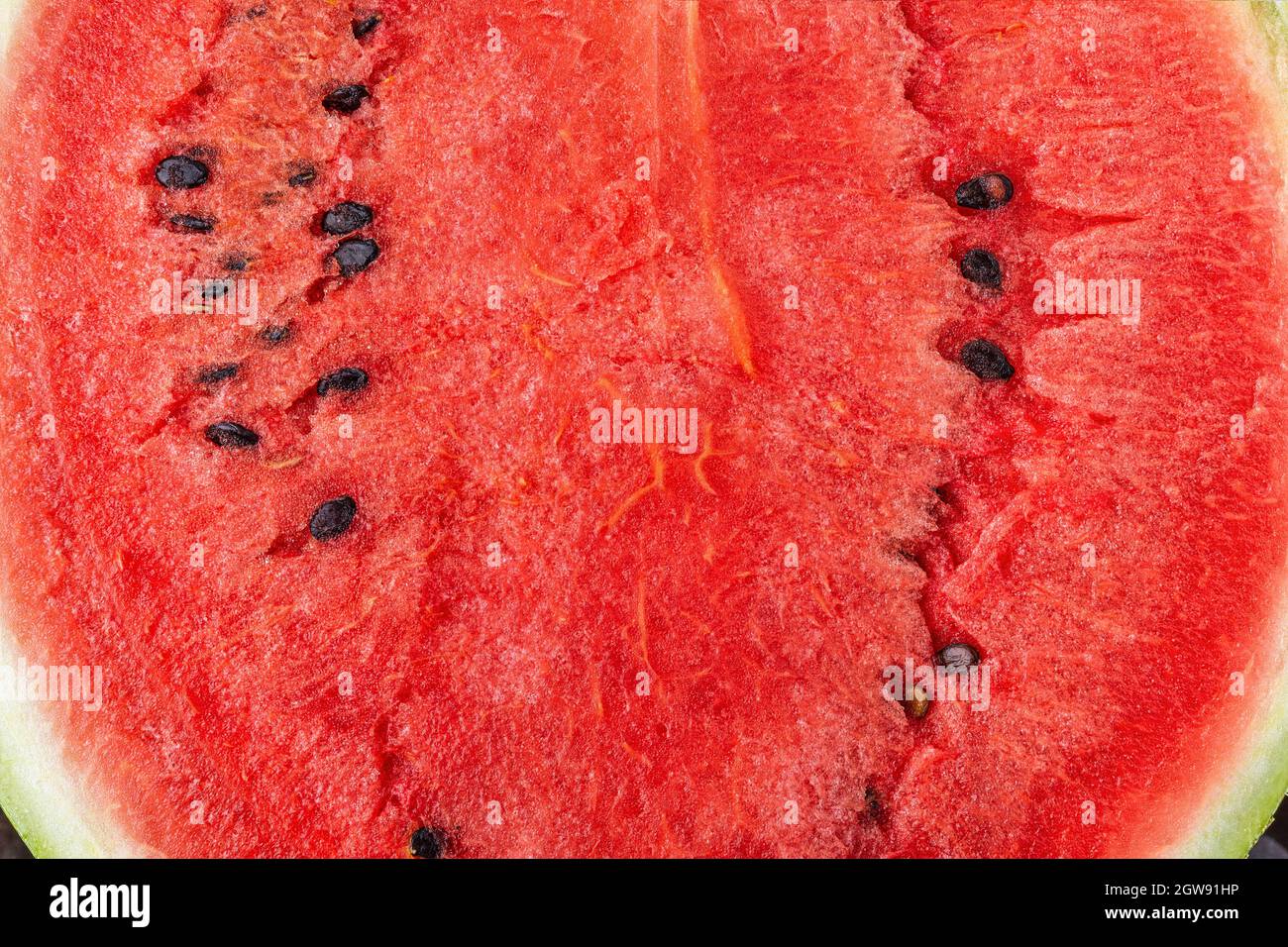 Cocomero succoso maturo con grana macro semi scuri. Primo piano con cocomero rosso dolce appena tagliato. Metà della deliziosa polpa di melone d'acqua biologica. Macro. Foto Stock