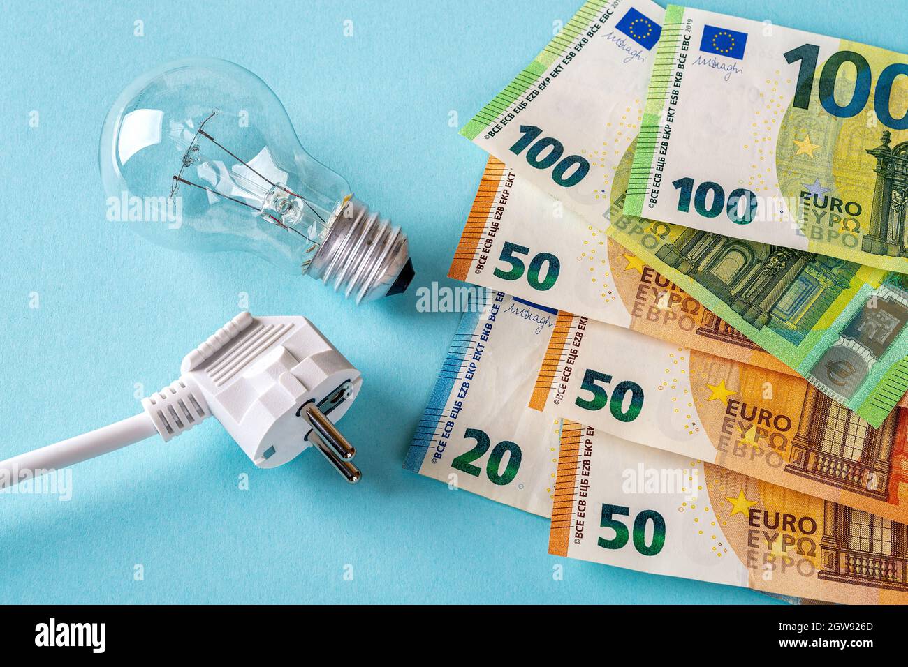 Spina elettrica bianca, lampadina e banconote in euro su sfondo blu. Aumento del costo dell'elettricità, aumento dei prezzi dell'elettricità. Foto Stock