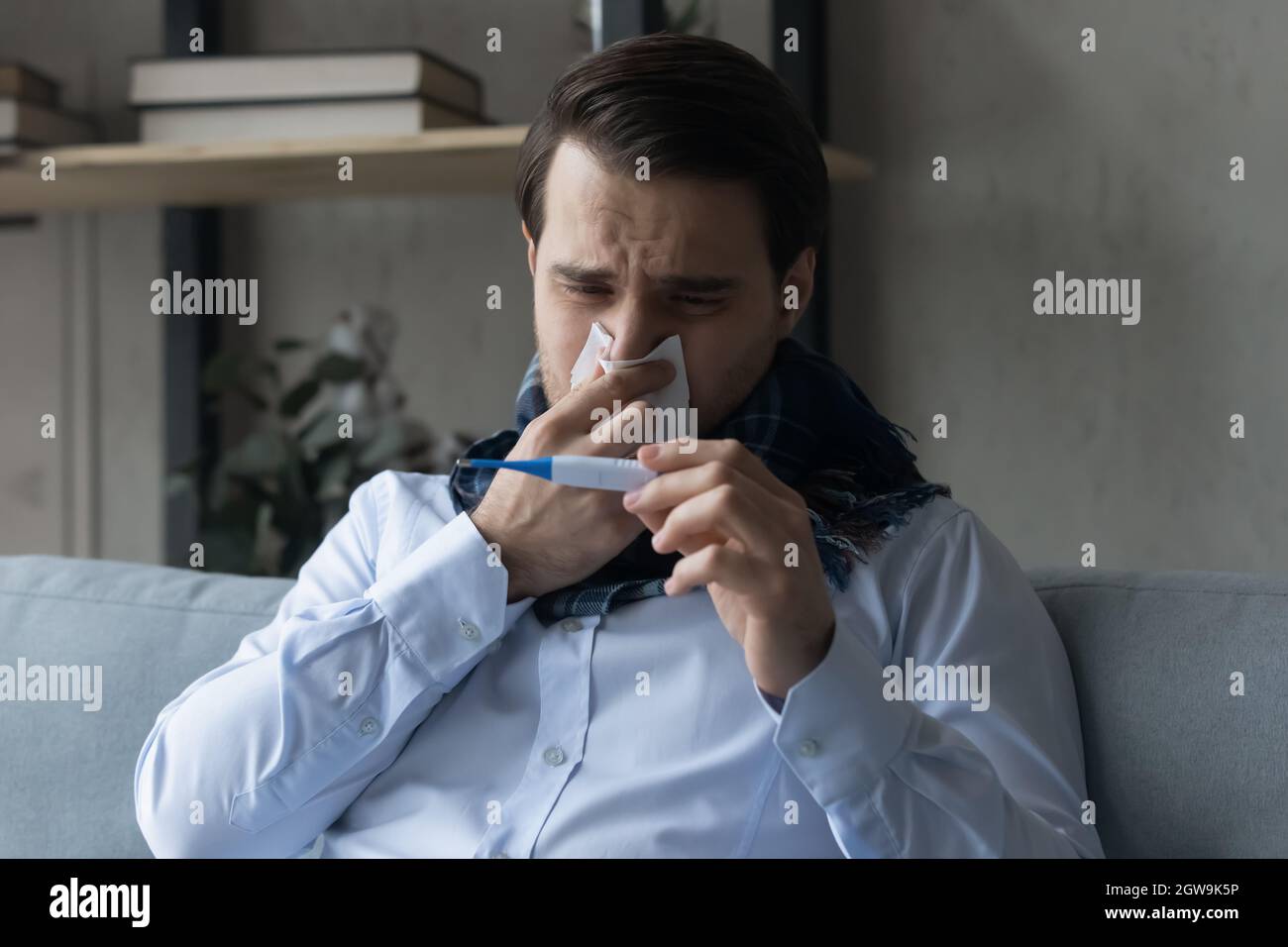 Primo piano uomo malato che soffia il naso, misurando la temperatura con termometro Foto Stock