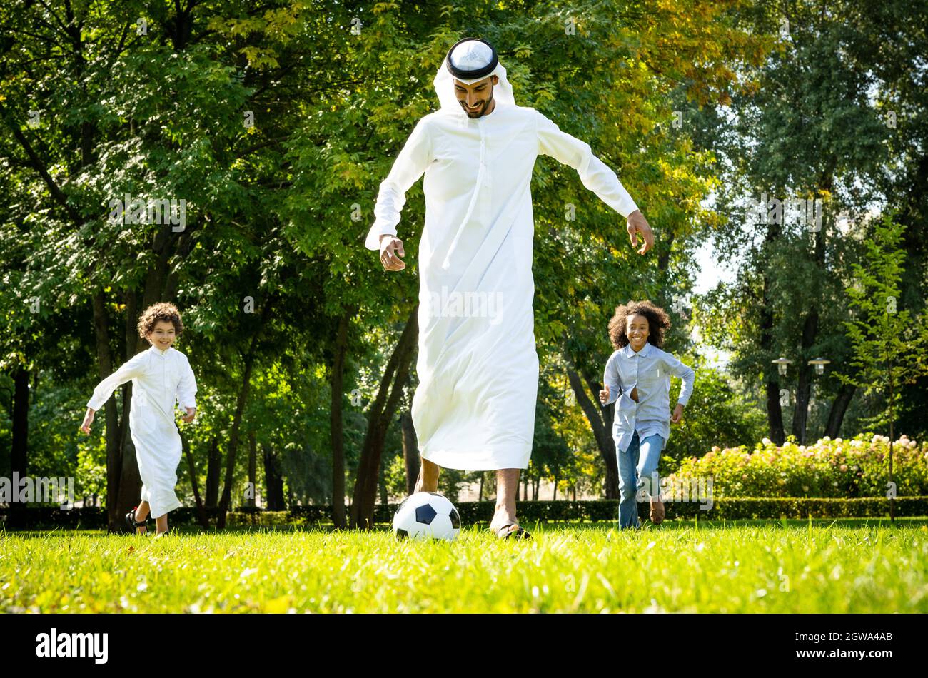 immagine cinematografica di una famiglia degli emirates che trascorre del tempo al parco. Fratello e sorella che giocano a calcio in erba Foto Stock