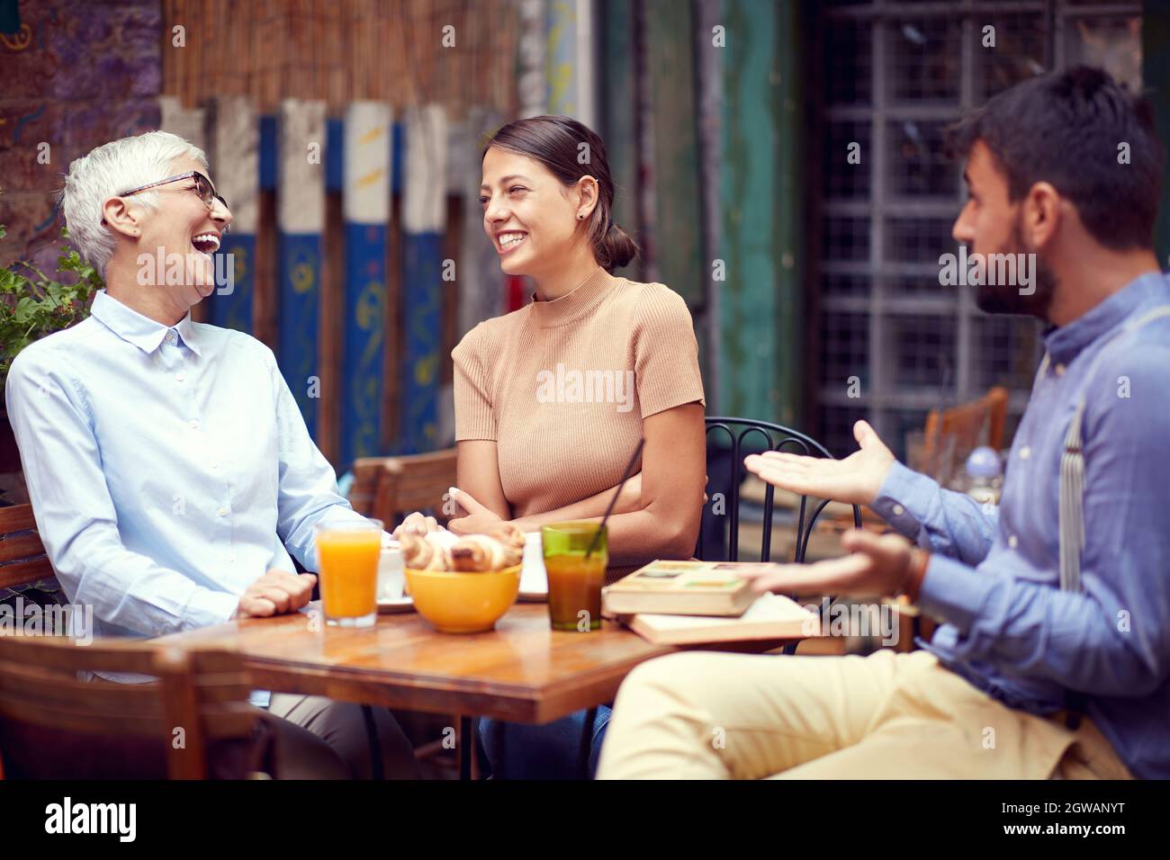 due donne, giovani adulti e anziani, che si divertono con il ragazzo della barba, si guardano, ridendo, sorridendo. luogo pubblico, bar all'aperto Foto Stock